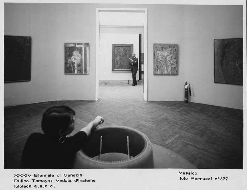 Black and white photo of Carla sitting in a gallery with Fernando Gamboa standing in a doorway during the Venice Biennale, 1968.
